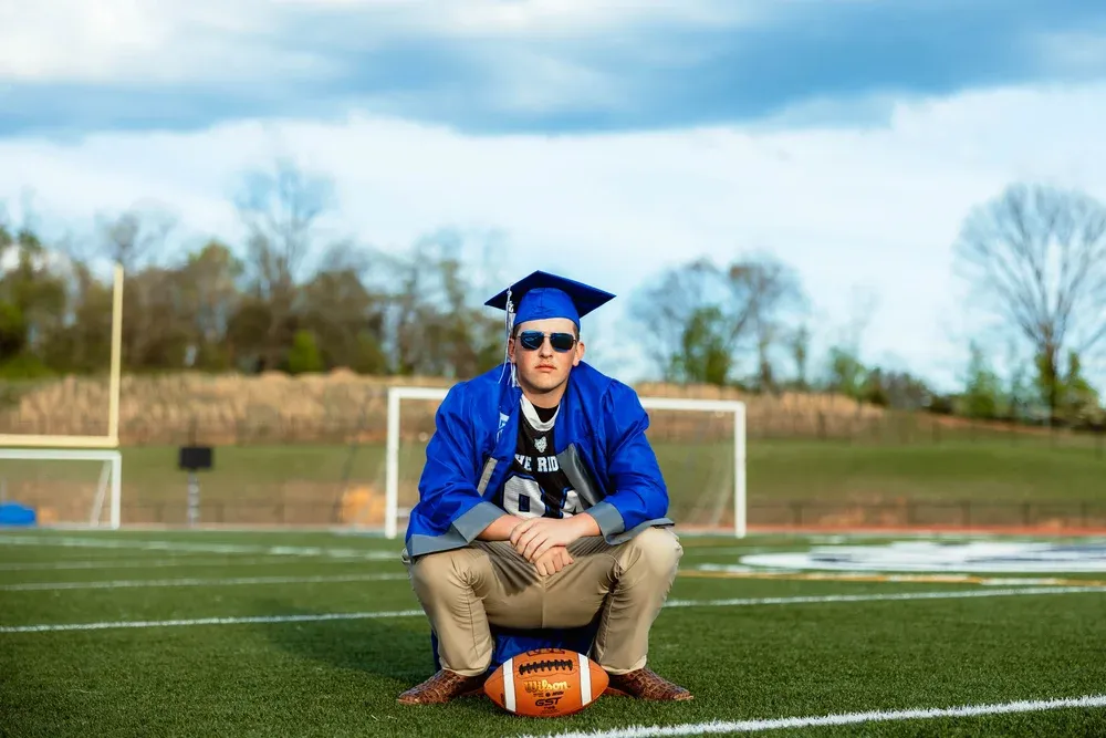 Graduate in cap and gown crouched on the football field