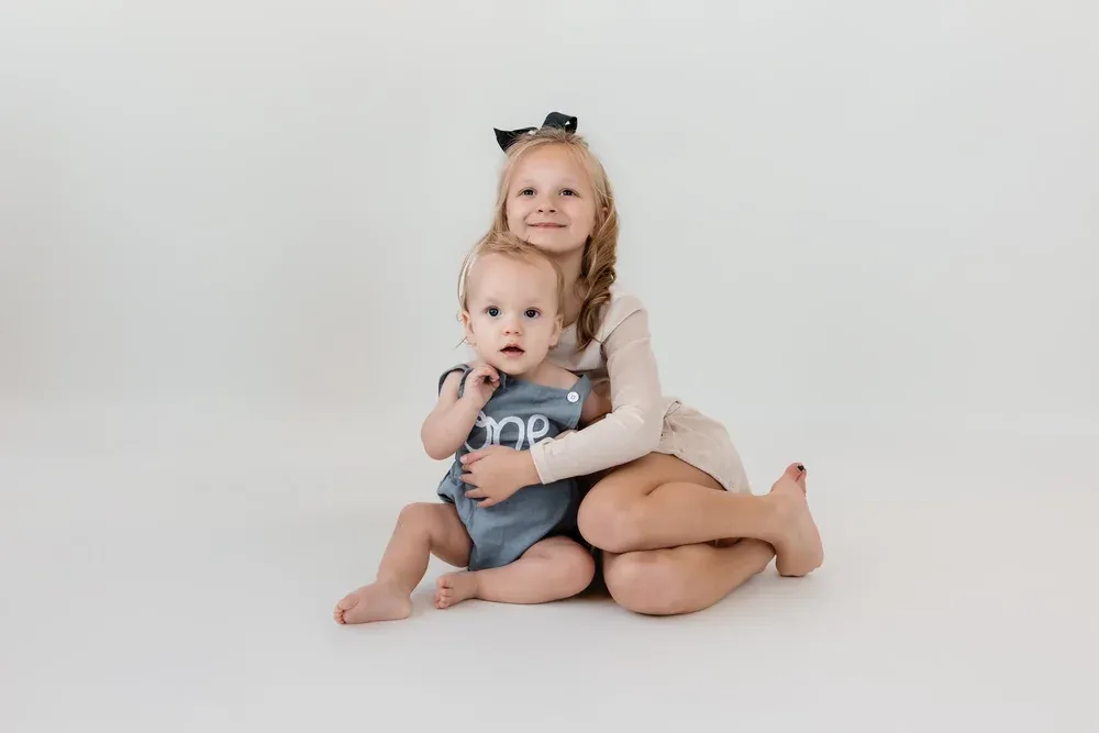 Two sisters sitting together for a first birthday portrait