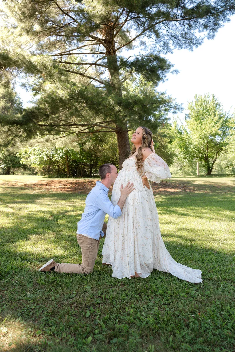 Husband kissing his wife's belly under a tree during a maternity session