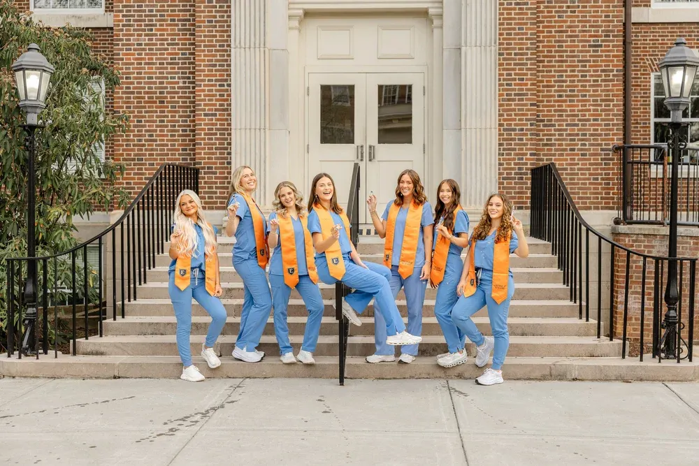 Group of nursing school graduates in scrubs and stoles on campus steps