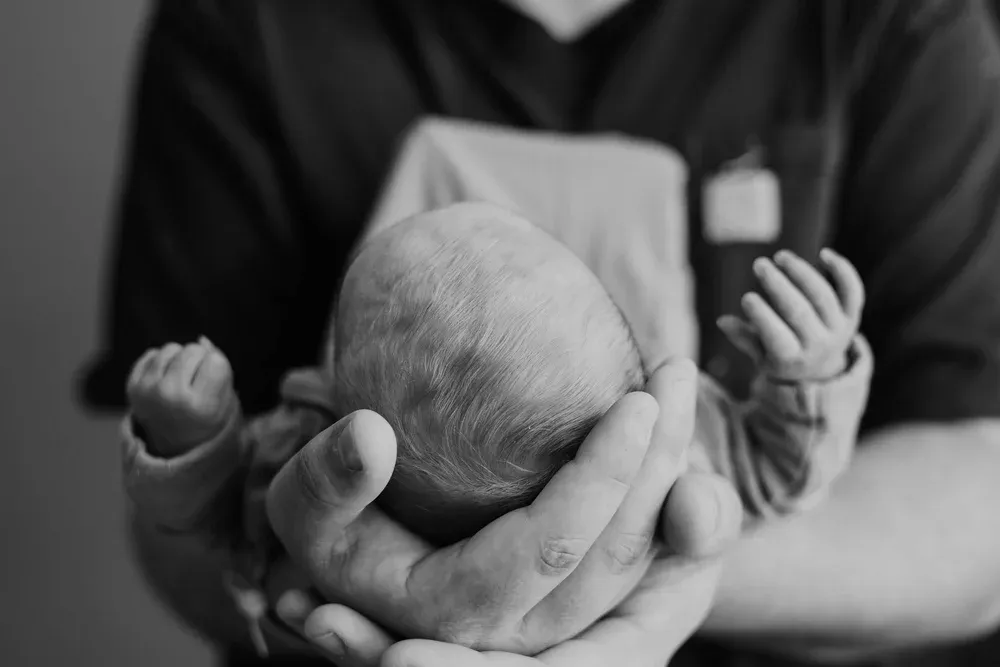 Newborn's head cradled gently in his father's hands, black and white