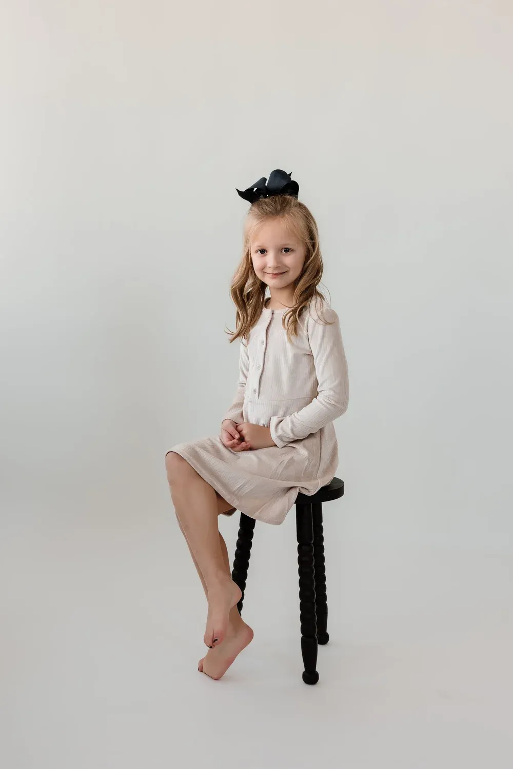 Young girl in a cream dress sitting on a stool in the studio