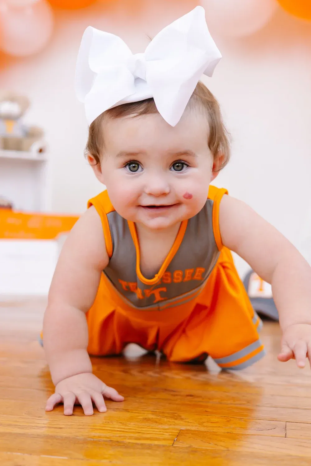 Baby crawling in a Tennessee-themed first birthday outfit with a big bow
