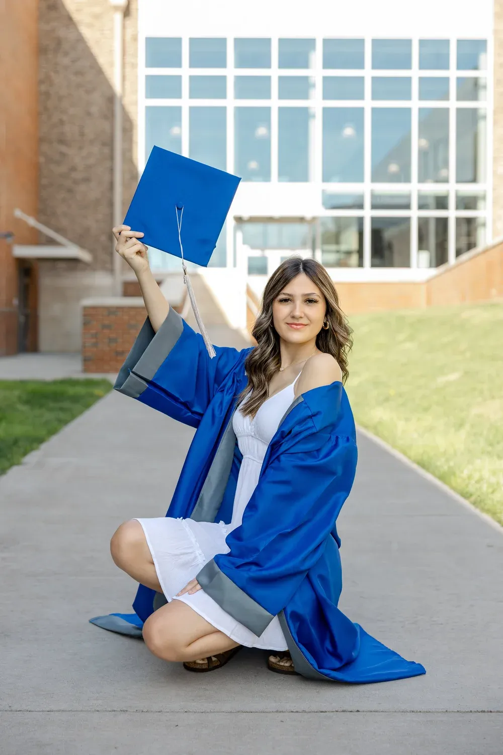 Graduate kneeling and holding her cap up on a campus walkway