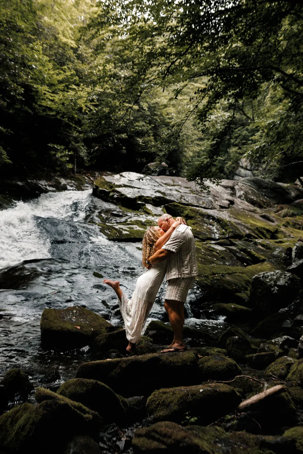 Couple embracing on moss-covered rocks beside a Smoky Mountains waterfall
