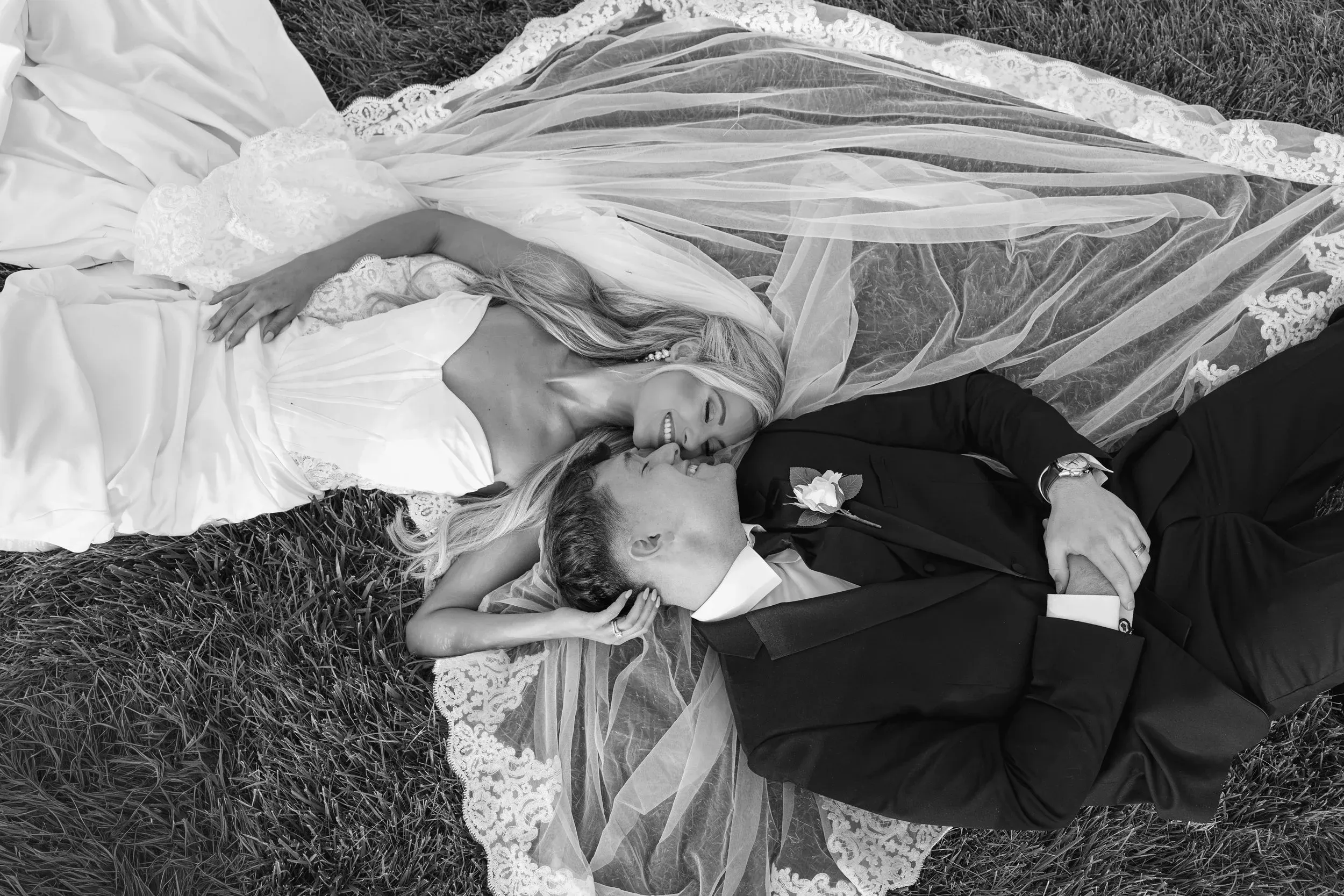 Bride and groom laughing together in the grass under her veil