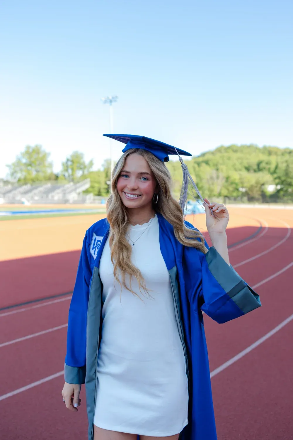 Graduate smiling on the track, holding her cap by the tassel