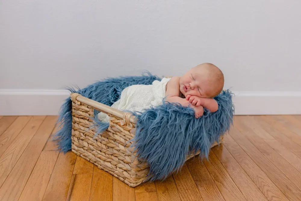 Sleeping newborn curled up in a woven basket with a blue fur blanket