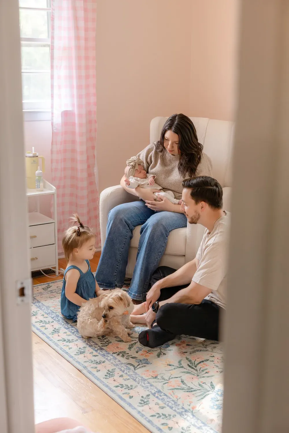 Family with their dog on the floor of a nursery, seen through a doorway