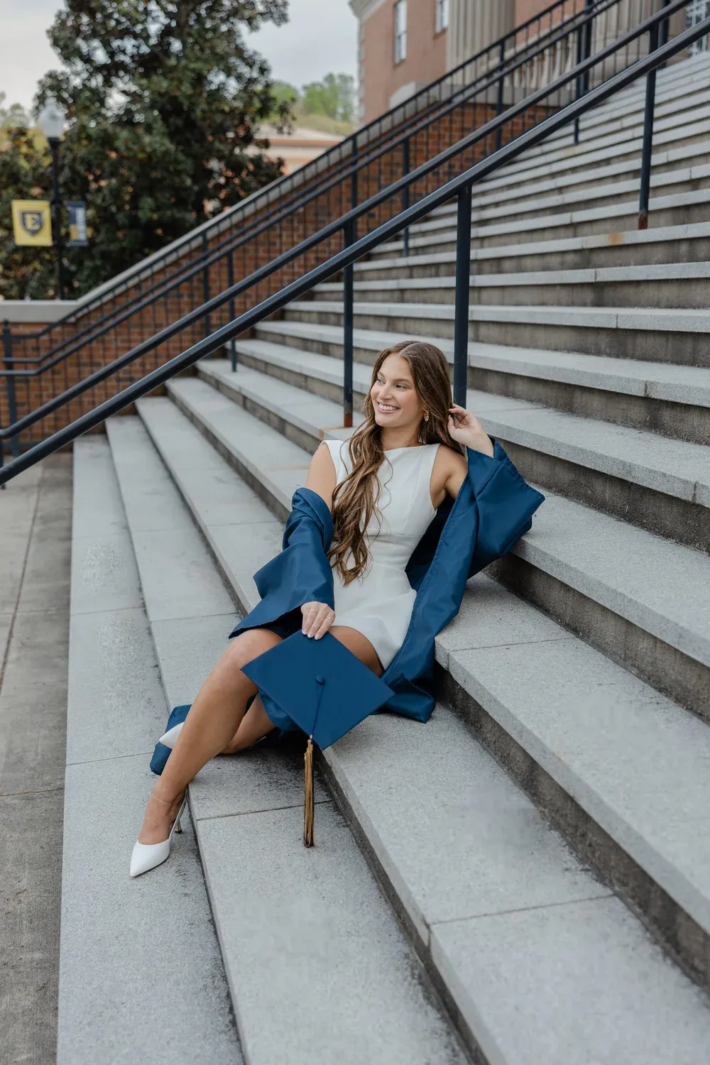 Graduate smiling beside a campus column, holding her Bachelor of Science sash