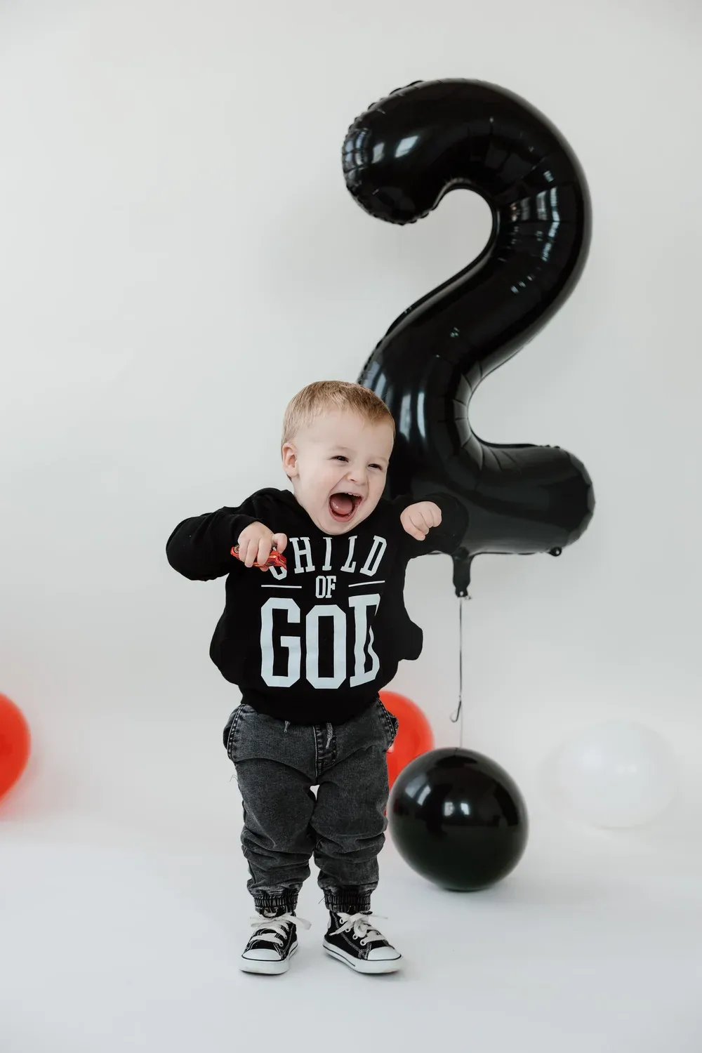 Toddler laughing and jumping in front of a birthday balloon backdrop