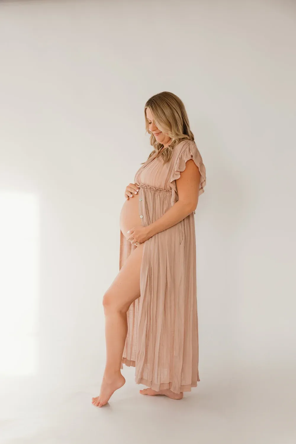 Expectant mother in a flowing blush dress, studio portrait